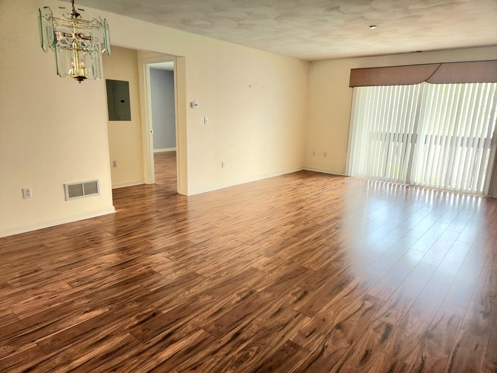Empty living room with wood flooring, a glass chandelier, and sliding doors with vertical blinds.