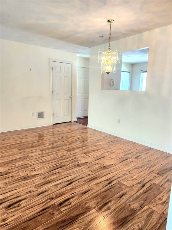 Empty room with wood-look plank flooring, a chandelier, and a large wall mirror.
