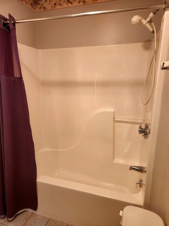 Bathroom with a cream tub and shower, handheld showerhead, and dark purple curtain.