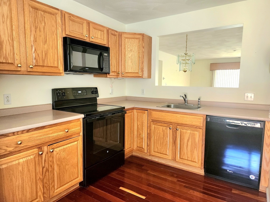 Kitchen with honey-colored cabinets, black appliances, pale countertops, and dark hardwood flooring.