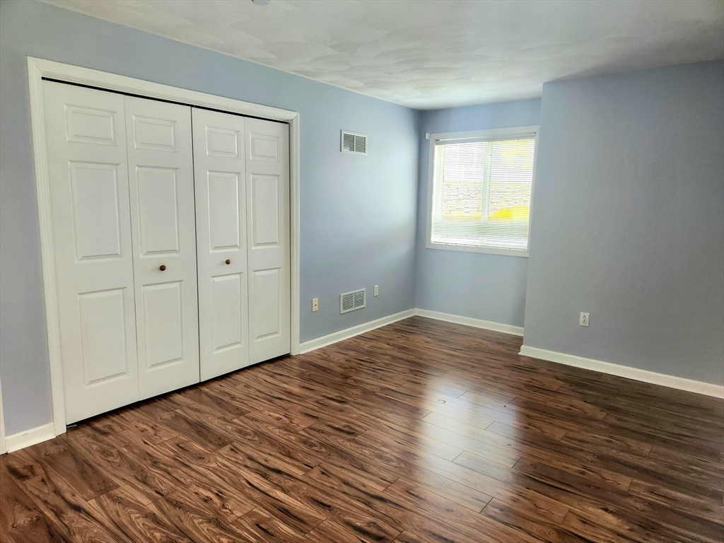 Empty bedroom with white closet doors, a window with blinds, and dark wood-look flooring.