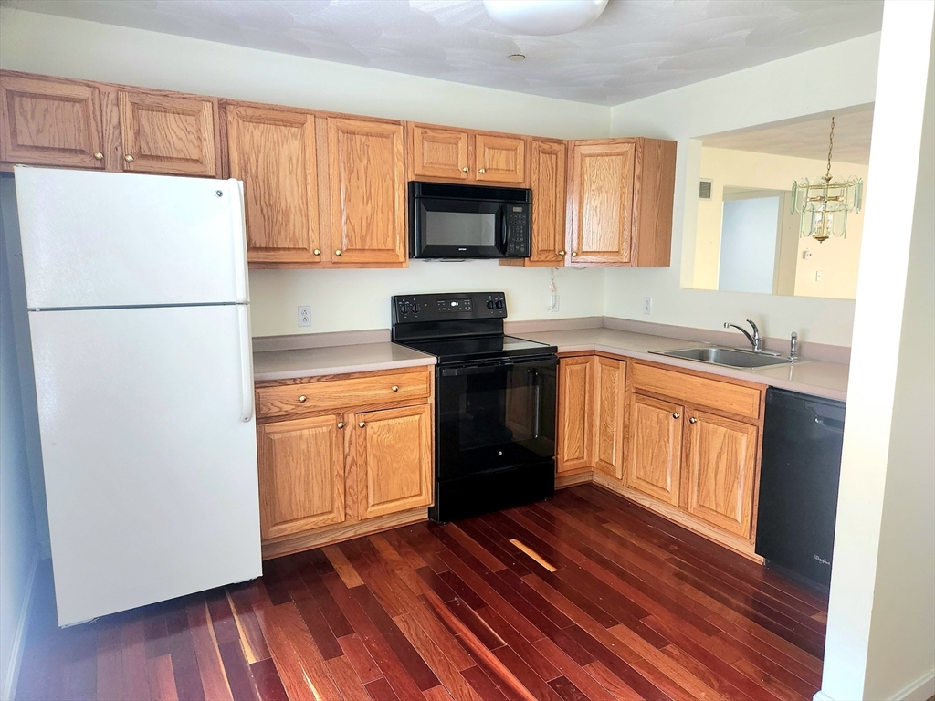 Kitchen with honey-toned wood cabinets, dark appliances, and hardwood floors.