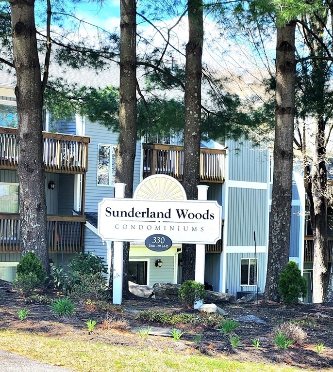 Sunderland Woods condominium entrance sign in front of the building, framed by tall pine trees.