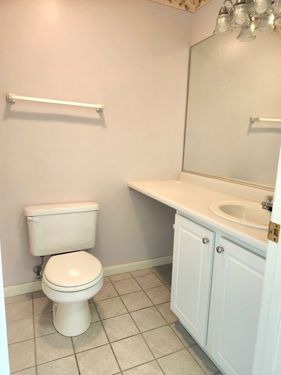 Bathroom with a white toilet, vanity, and large mirror above beige tile flooring.
