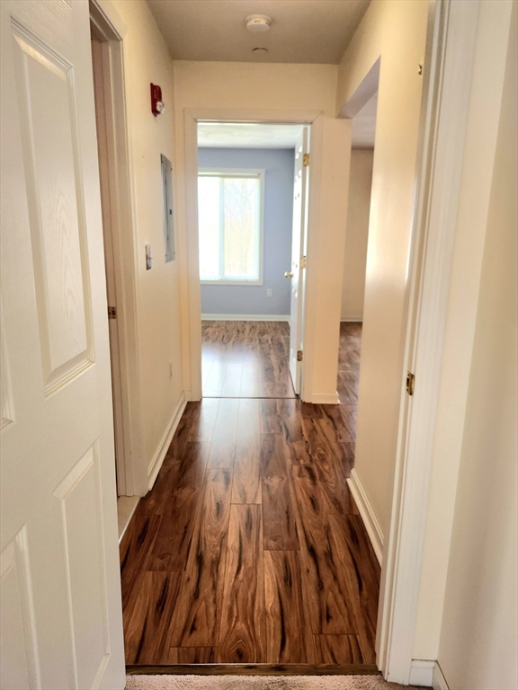 Unfurnished hallway with glossy wood-look floors and a bright room at the far end.