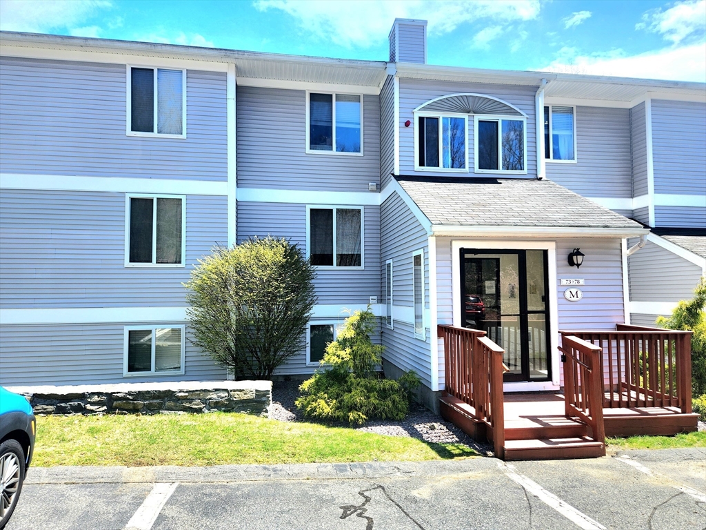 Gray-sided condominium building with a raised wooden entry deck and glass double doors.