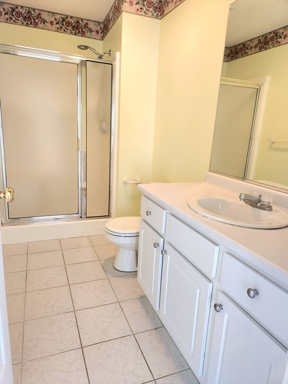 Bathroom with glass shower enclosure, white vanity, and light tiled floor.