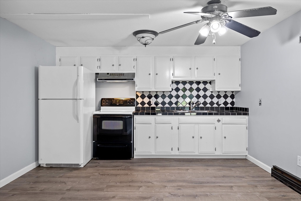 Kitchen with white cabinets, black-and-white diamond backsplash, and gray wood-look flooring.