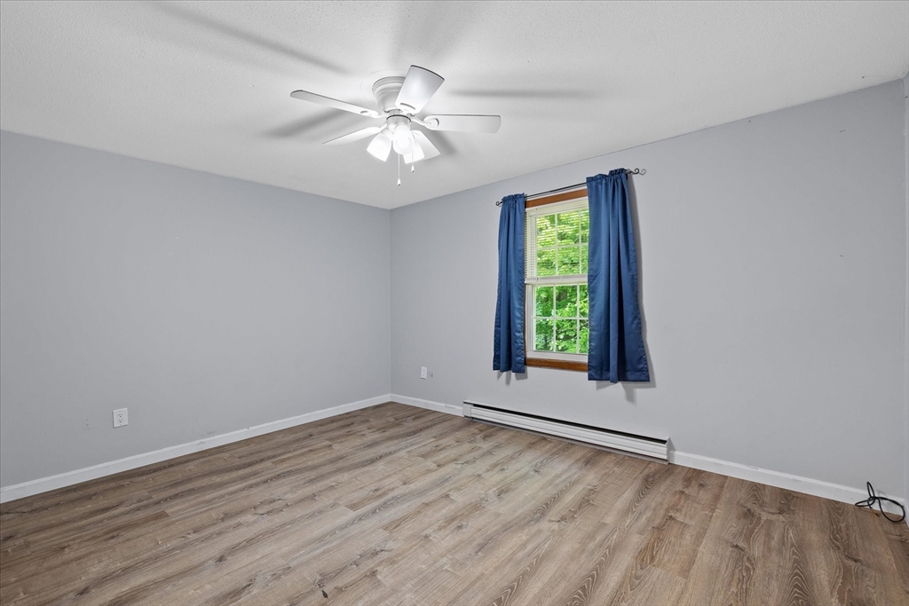 Empty bedroom with gray walls, wood-look flooring, blue curtains, and a ceiling fan.
