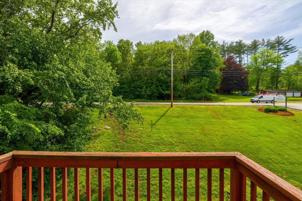 Deck overlooks a broad green lawn, roadside, and dense summer trees.