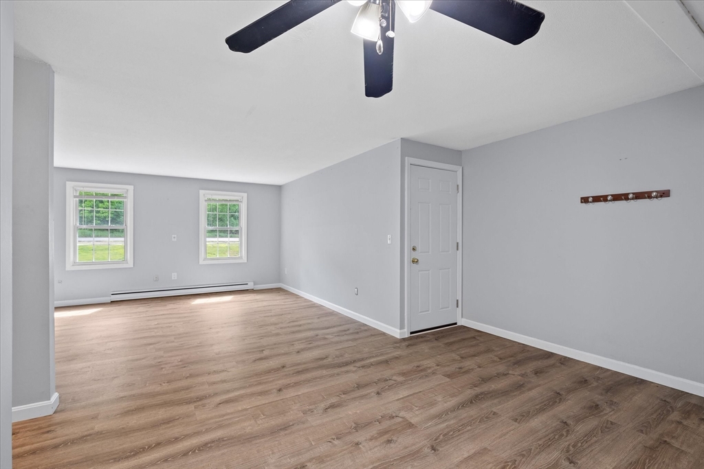 Empty room with wood-look flooring, two windows, a ceiling fan, and a baseboard heater.