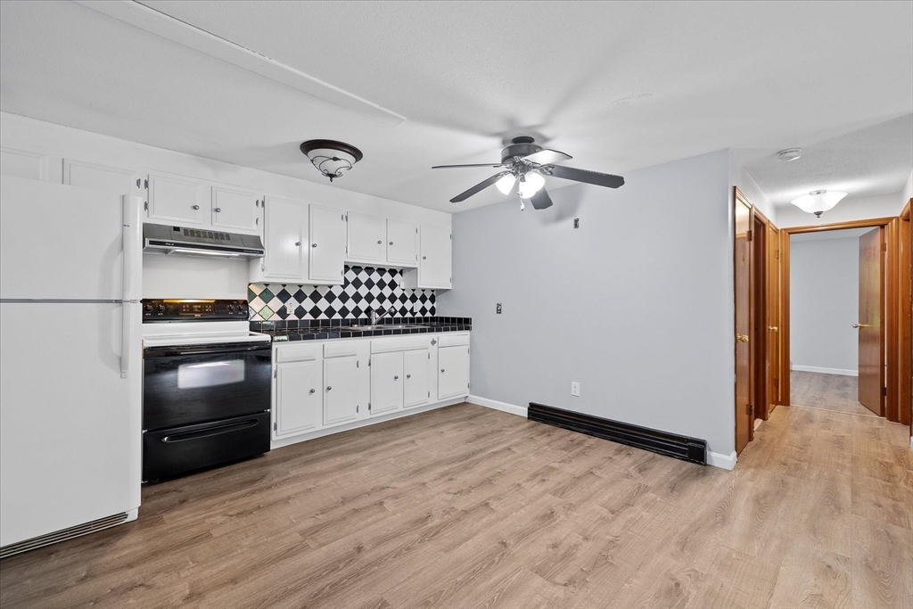 Unfurnished kitchen with white cabinets, black appliances, diamond-pattern backsplash, and wood-look floors.