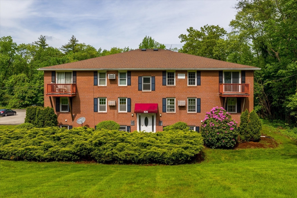 Red-brick apartment building with two balconies, a red 325 entrance awning, and landscaped lawn.