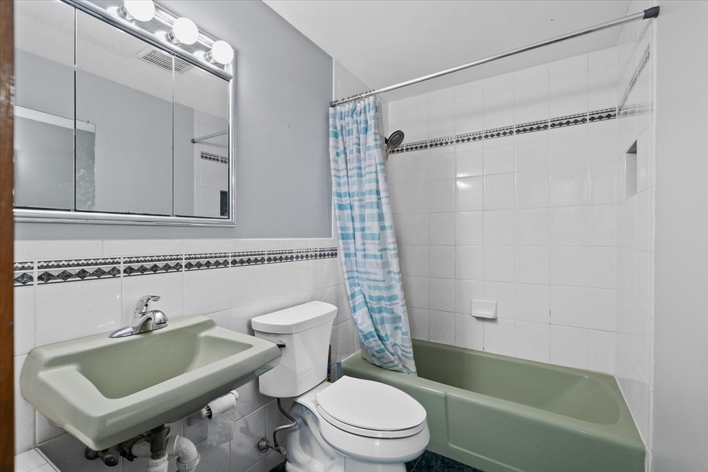 Bathroom with a green bathtub and matching sink, white tiled walls, and a blue-and-white shower curtain.