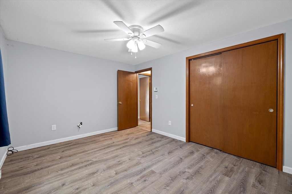 Empty bedroom with wood-look flooring, a ceiling fan, and large wooden closet doors.