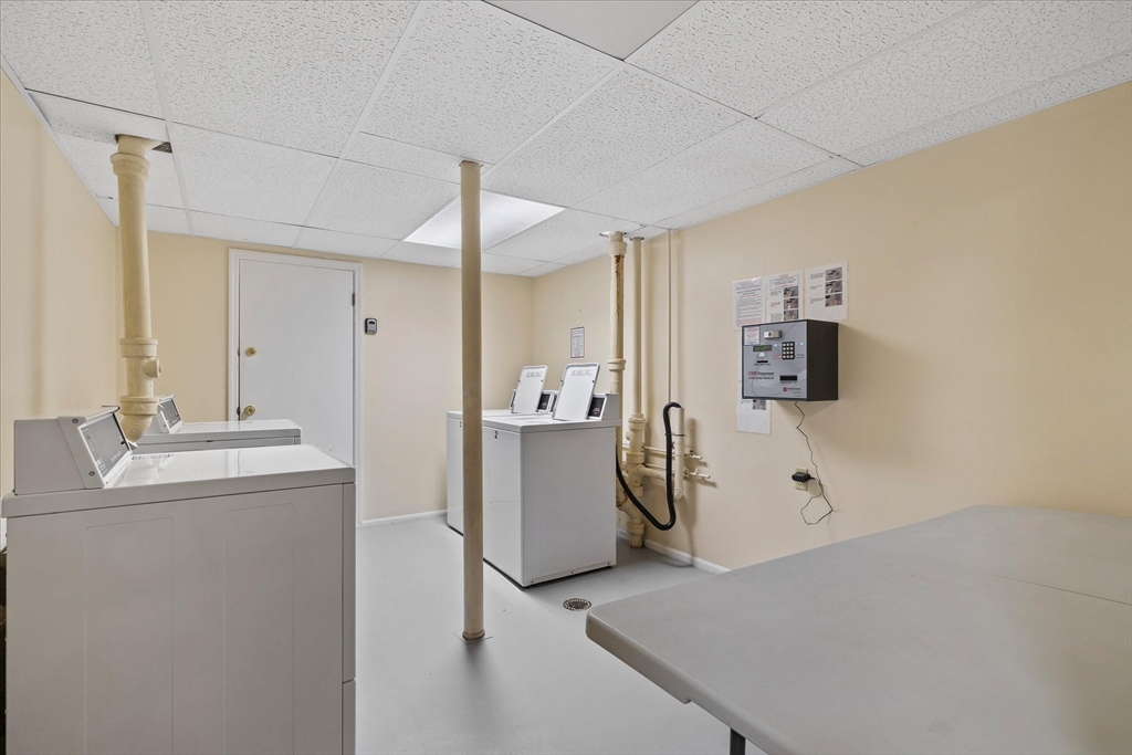 Shared laundry room with white machines, exposed plumbing, and a large folding table.