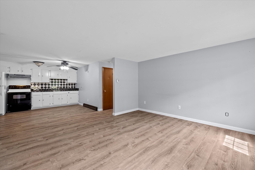 Open living area with wood-look floors and a white kitchen featuring a black-and-white tile backsplash.