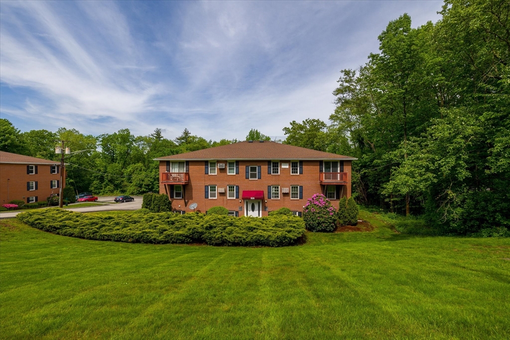 Two-story brick apartment building with end balconies, trimmed shrubs, and a broad green lawn.