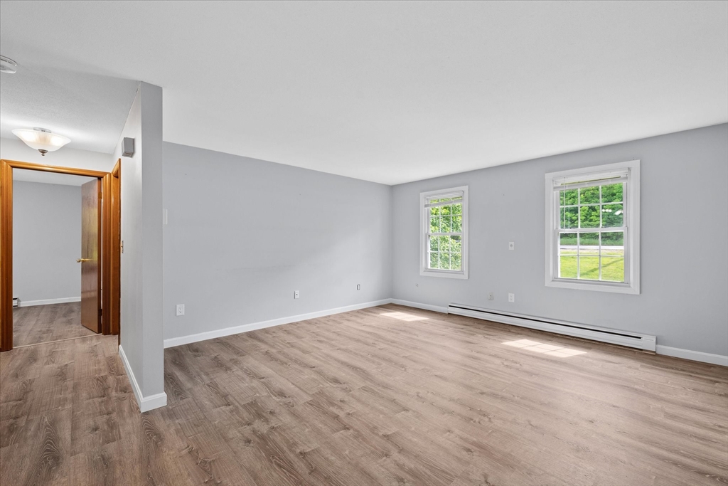 Empty living room with gray walls, wood-look flooring, and two sunlit windows.