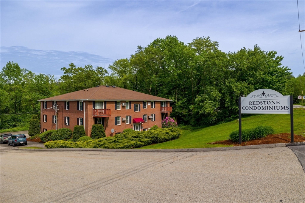 Red brick condominium building with balconies and a Redstone Condominiums sign beside the road.