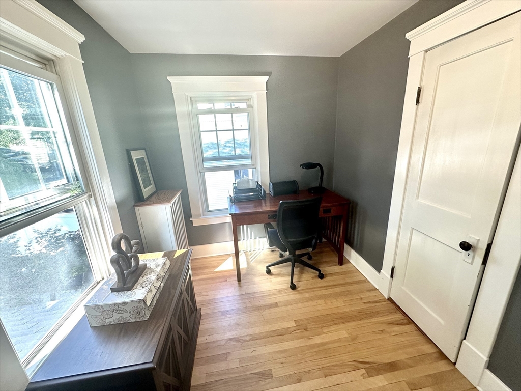Home office with a wooden desk, gray walls, hardwood floors, and white-trimmed windows.