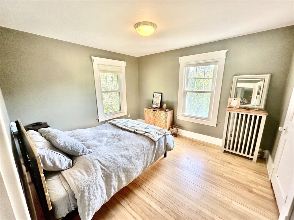 Bedroom with a gray bed, two white-trimmed windows, and hardwood floors.