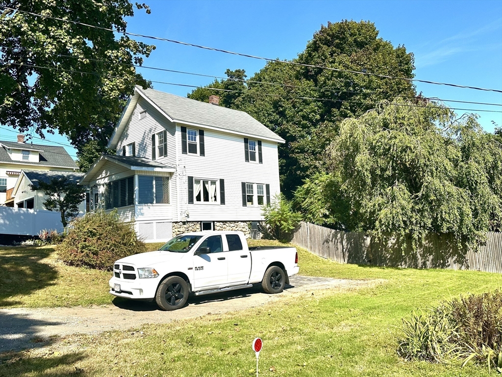 White two-story house with a stone foundation and covered porch, with a pickup truck parked in front.