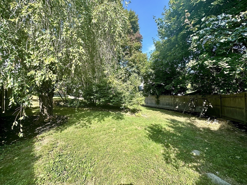 Backyard with a grassy lawn, mature trees, wooden privacy fence, and swing set.