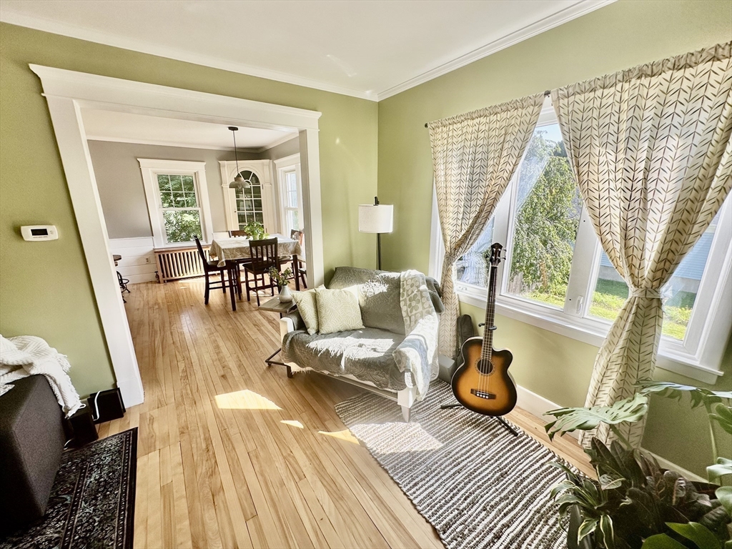 Living room with pale green walls, hardwood floors, large windows, and an adjoining dining room.