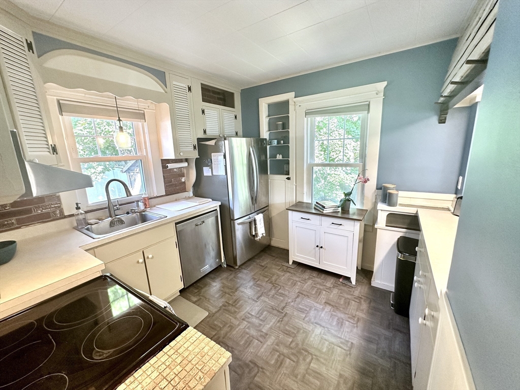 Kitchen with blue-green walls, white cabinetry, stainless steel appliances, and two bright windows.