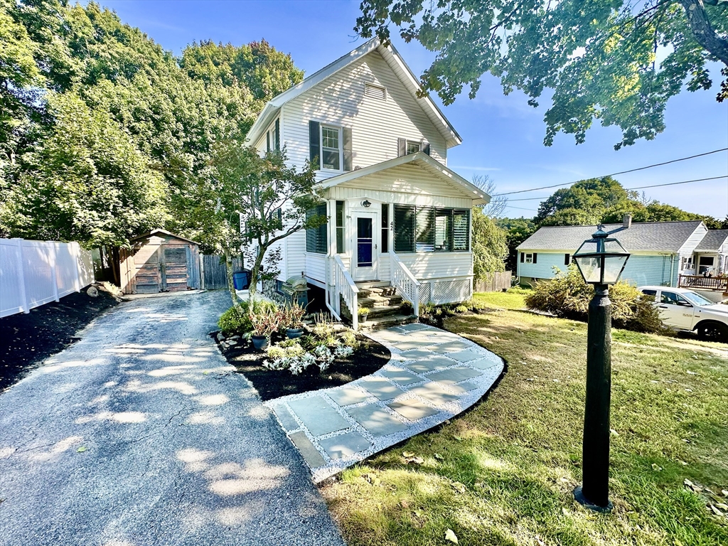 White two-story house with a covered porch, curved stone walkway, and landscaped front garden.