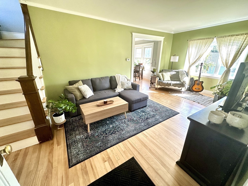 Living room with a dark sectional, patterned rug, hardwood floors, and a staircase.