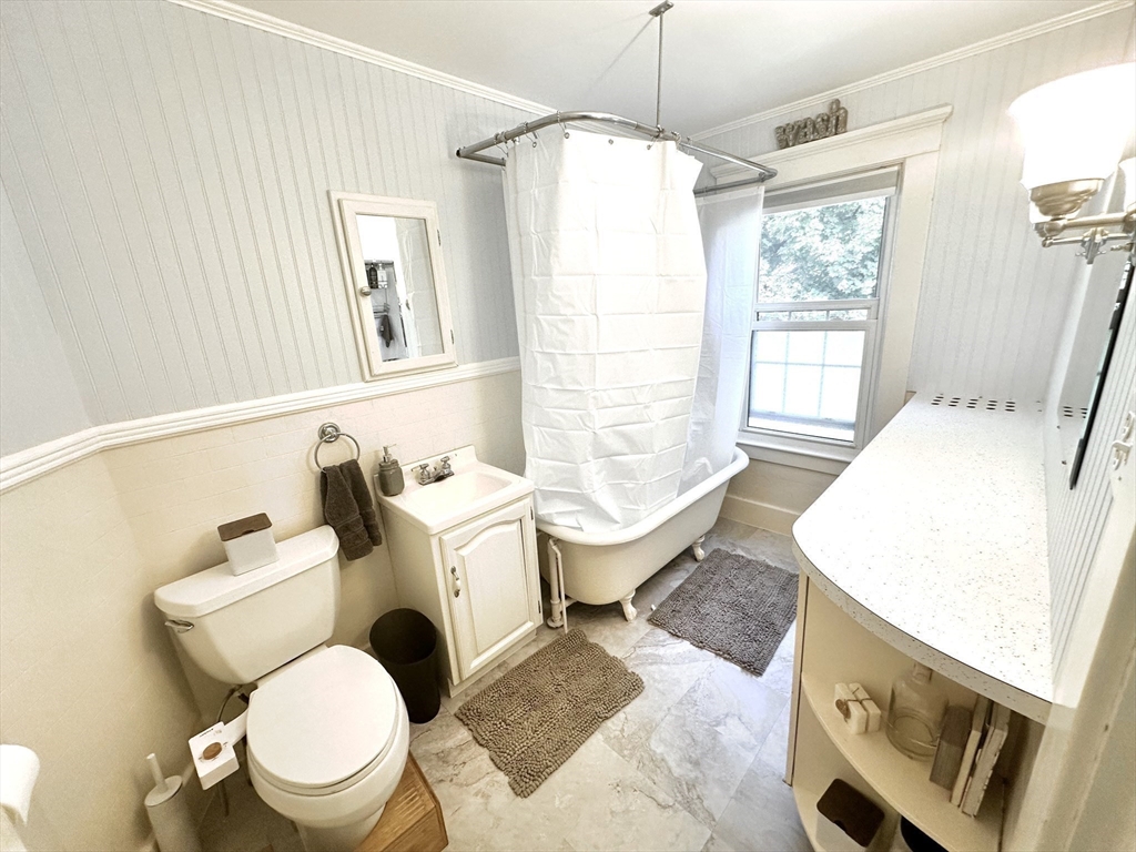Bright bathroom with a white bathtub, shower curtain, window, and long vanity.