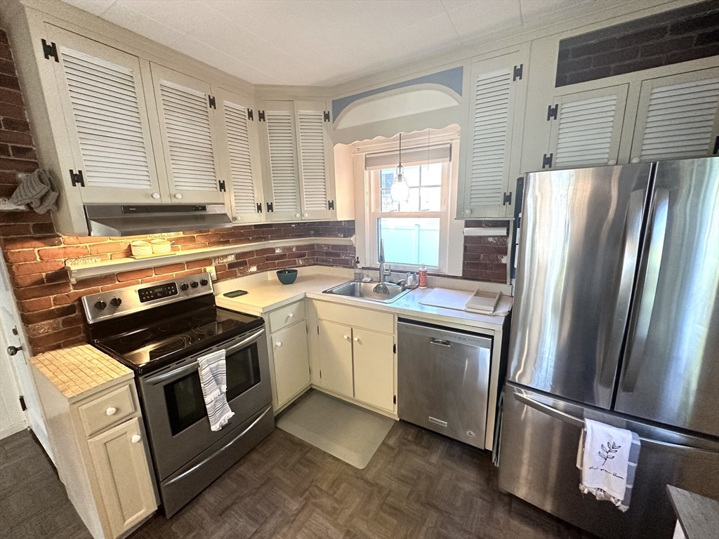 Kitchen with cream louvered cabinets, brick backsplash, and stainless steel appliances.