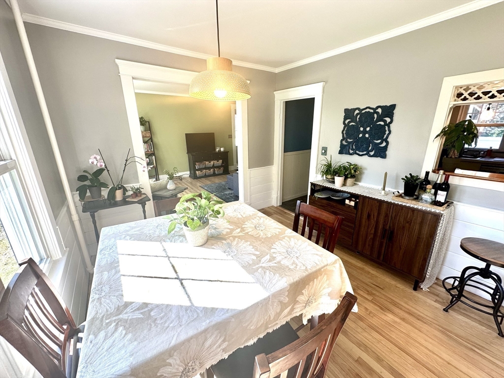 Dining room with a floral tablecloth, pendant light, and dark wood sideboard beside a wide living room doorway.