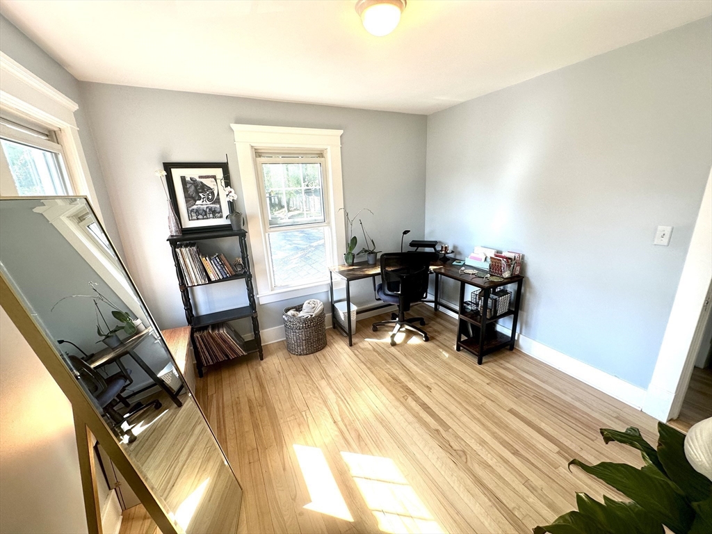 Home office with hardwood floors, a desk by the windows, and a large leaning mirror.