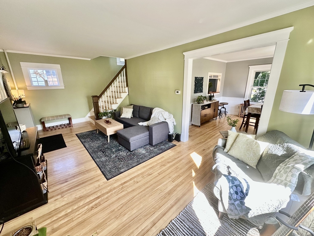 Living room with sage-green walls, hardwood floors, a gray sectional, and an open doorway to the dining area.