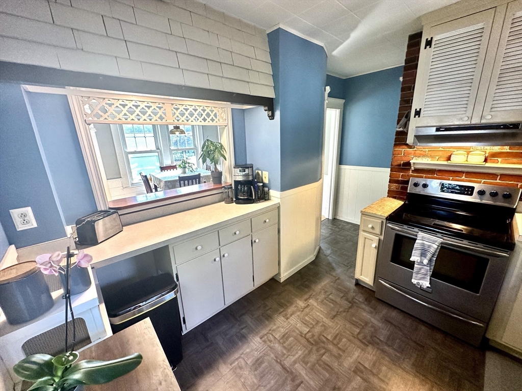 Kitchen with blue walls, white cabinetry, a stainless-steel range, and a pass-through to the dining area.