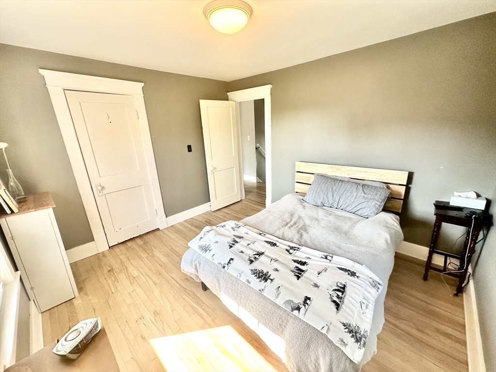 Bedroom with gray walls, light wood floors, and a bed with a slatted wood headboard.