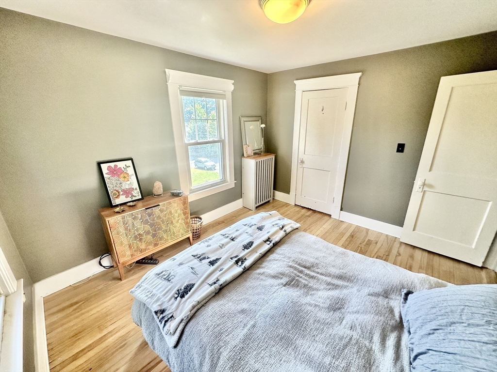 Furnished bedroom with hardwood floors, a tall window, and a decorative radiator cover.