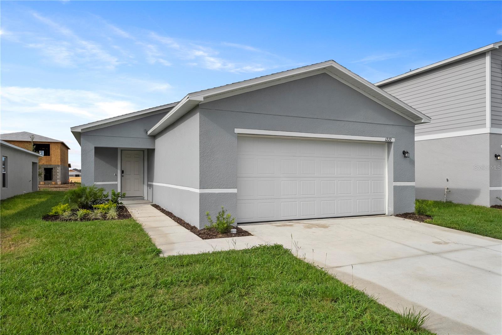 Gray single-story house with a white double garage door, driveway, and small landscaped garden.
