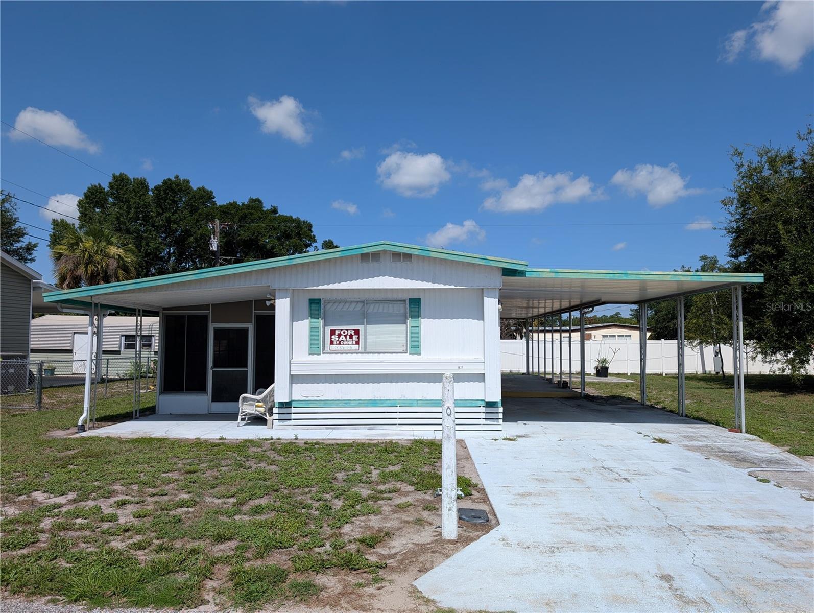 1627 Acacia Dr, a white manufactured home with turquoise trim and a long attached carport.
