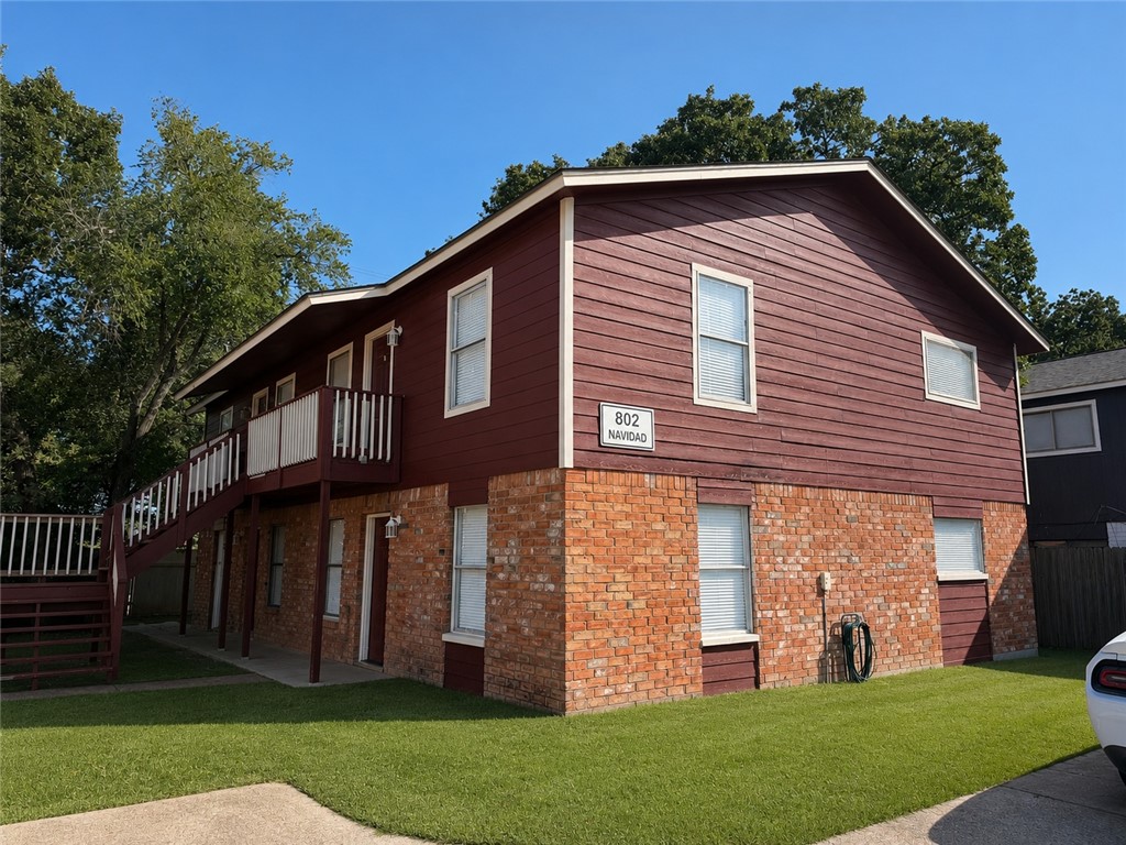 Two-story red-sided and brick house with an elevated porch and a sign reading 802 Navidad.