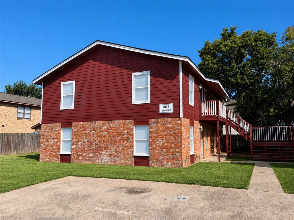 Red-sided two-story home with a brick lower level and raised wooden deck.