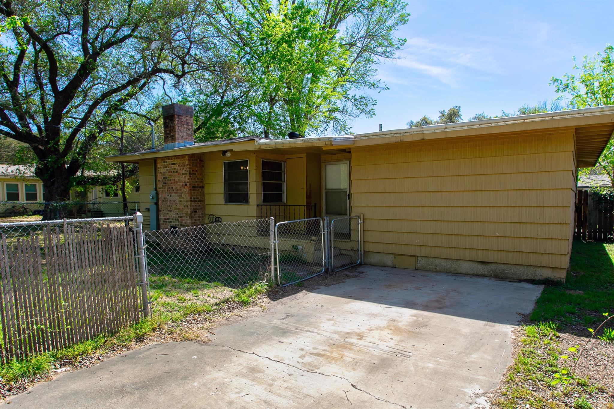 Rear of a yellow-sided house with a brick chimney, fenced patio, and concrete driveway.