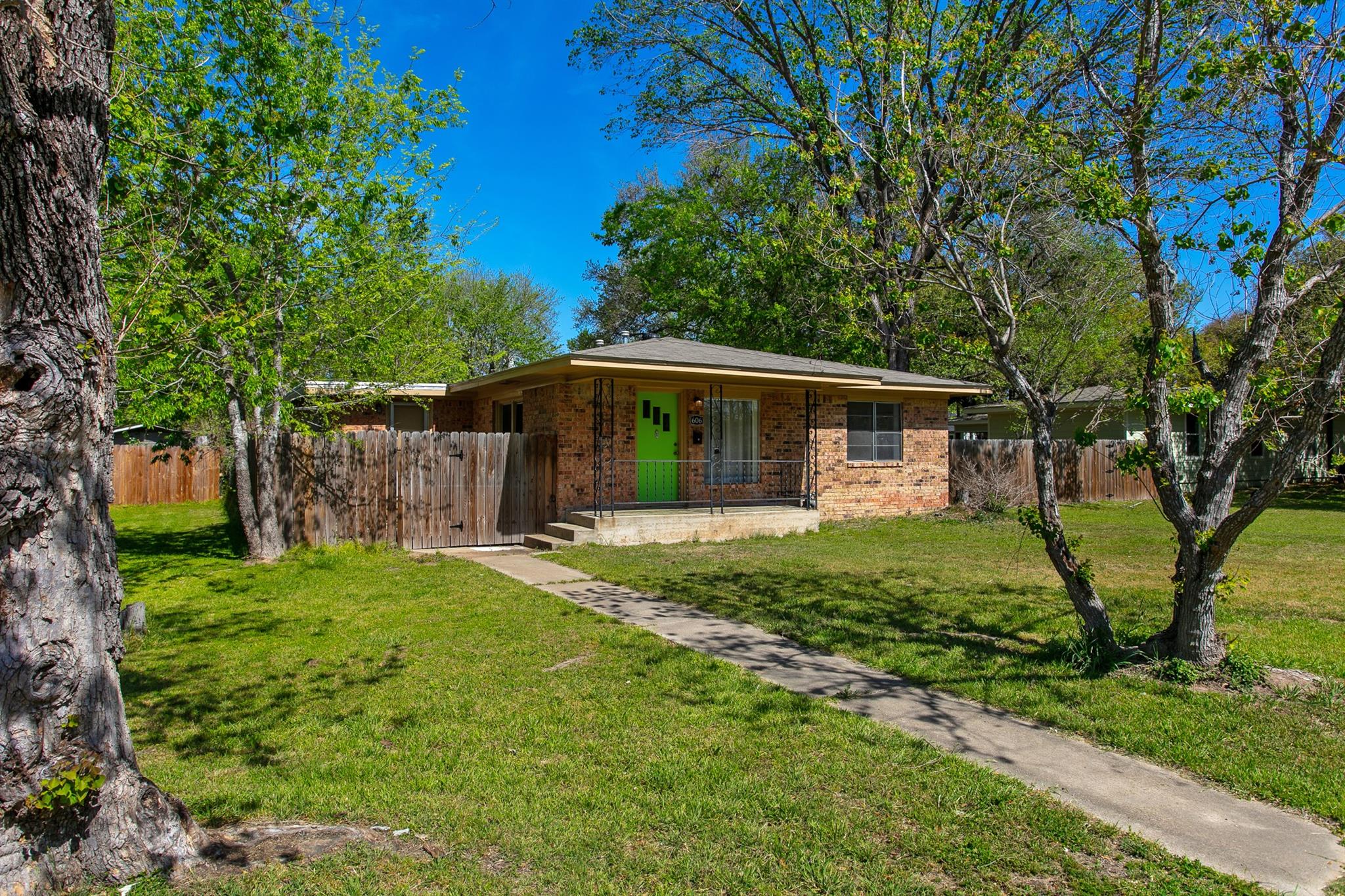Brick home with a bright green front door, covered porch, and mature trees.