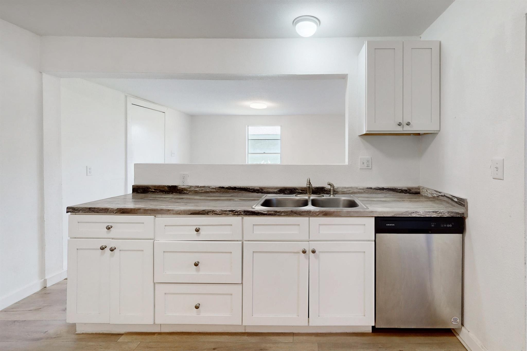 Kitchen with white cabinets, a double sink, mottled stone-look counters, and a stainless steel dishwasher.
