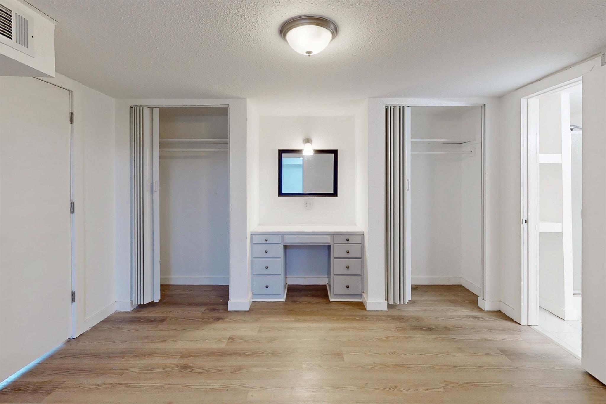Empty bedroom with two open closets, a built-in vanity, and wood-look flooring.