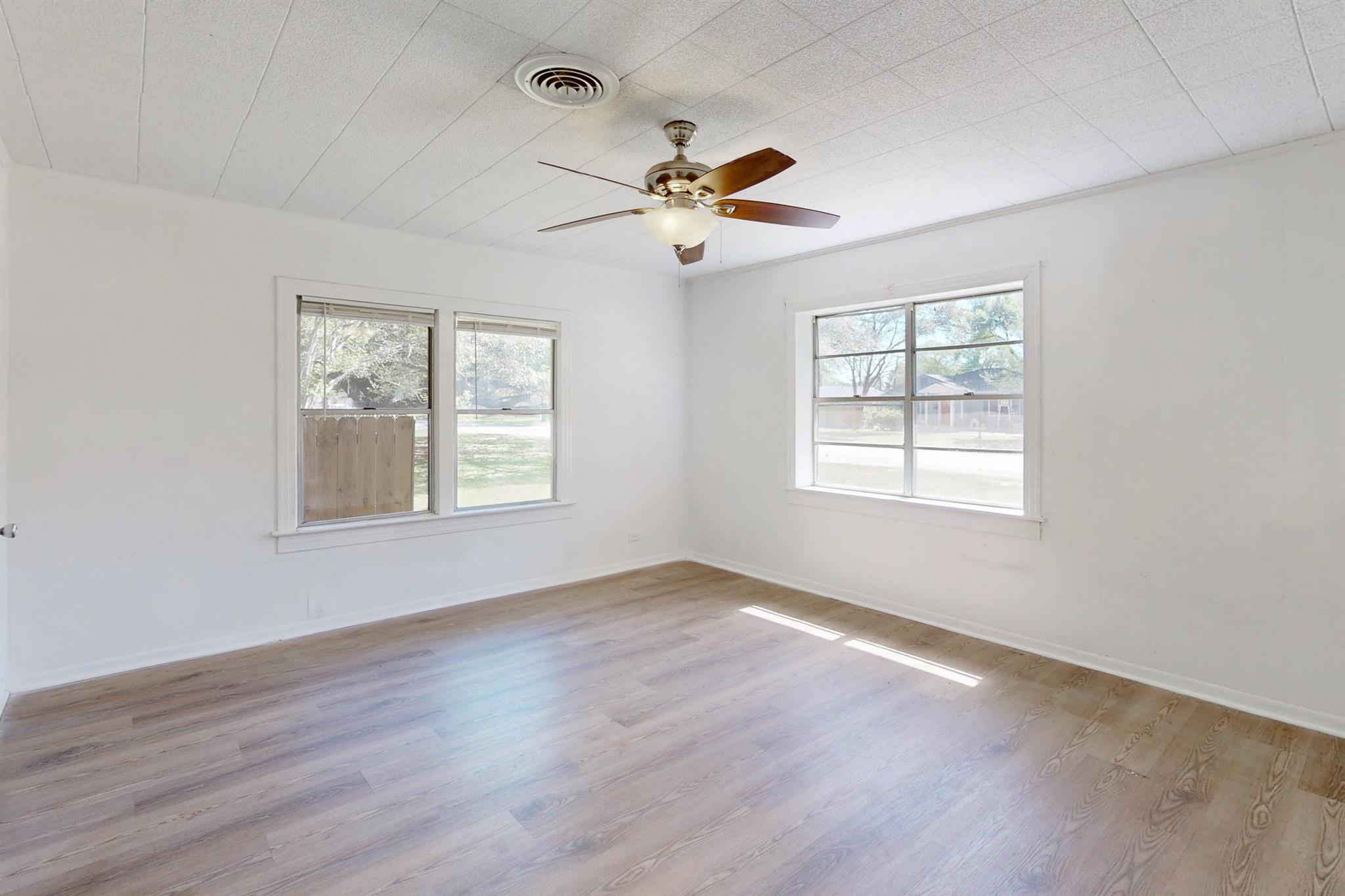 Empty room with light wood-look flooring, three windows, and a ceiling fan.