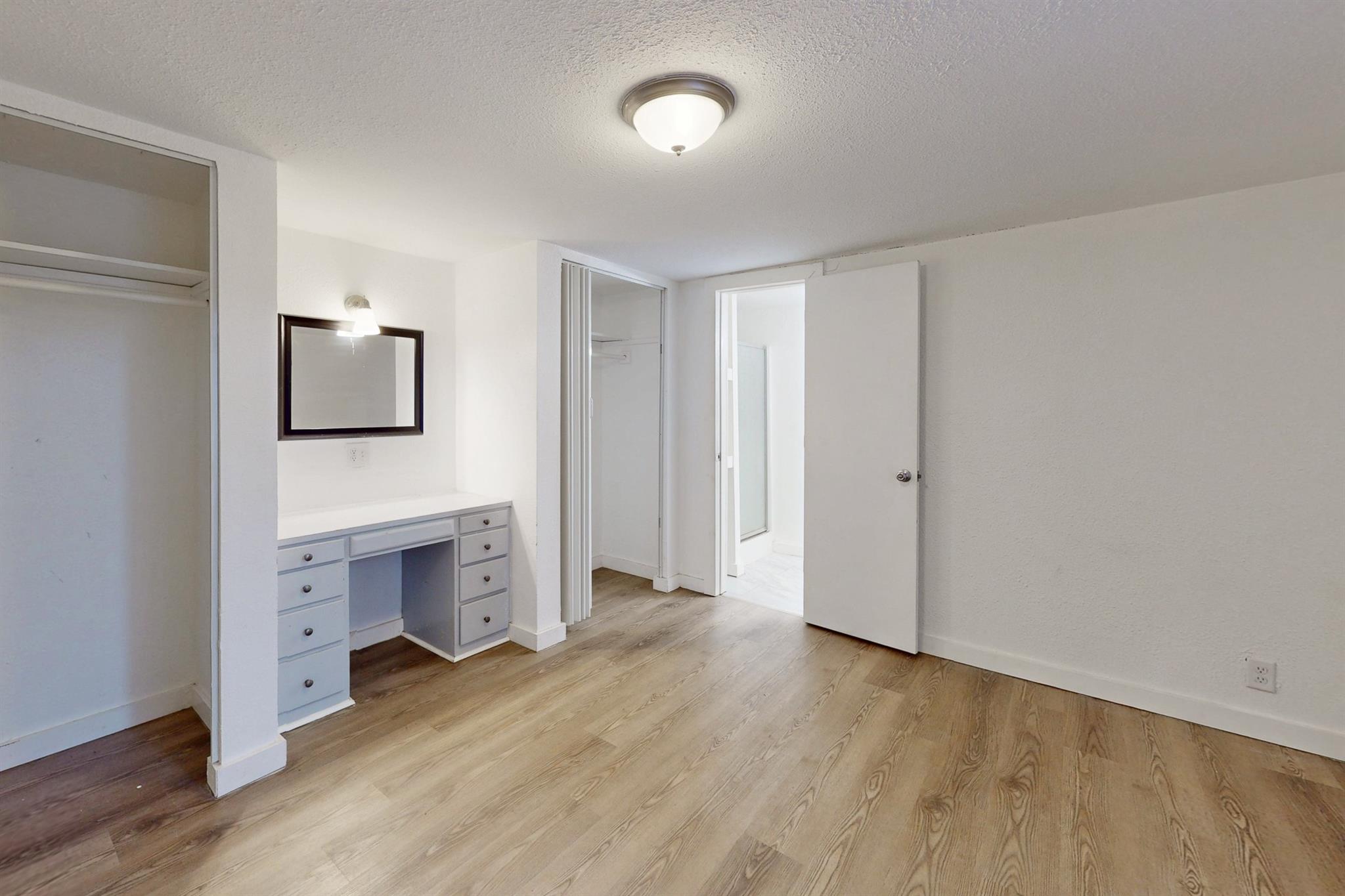 Empty bedroom with light wood floors, an open closet, and a built-in vanity.